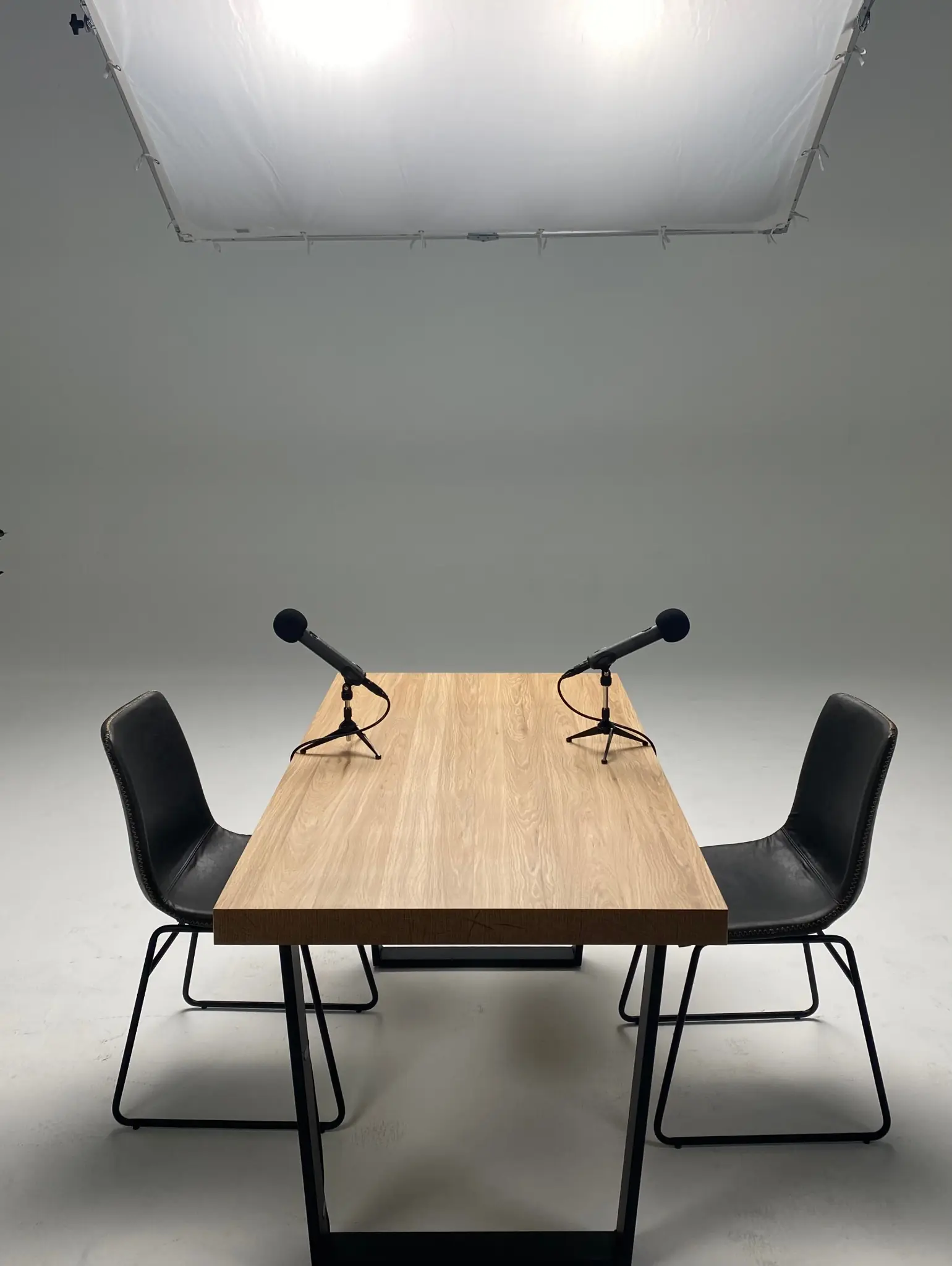 Two microphones and chairs arranged beneath a suspended diffusion frame for a recorded conversation